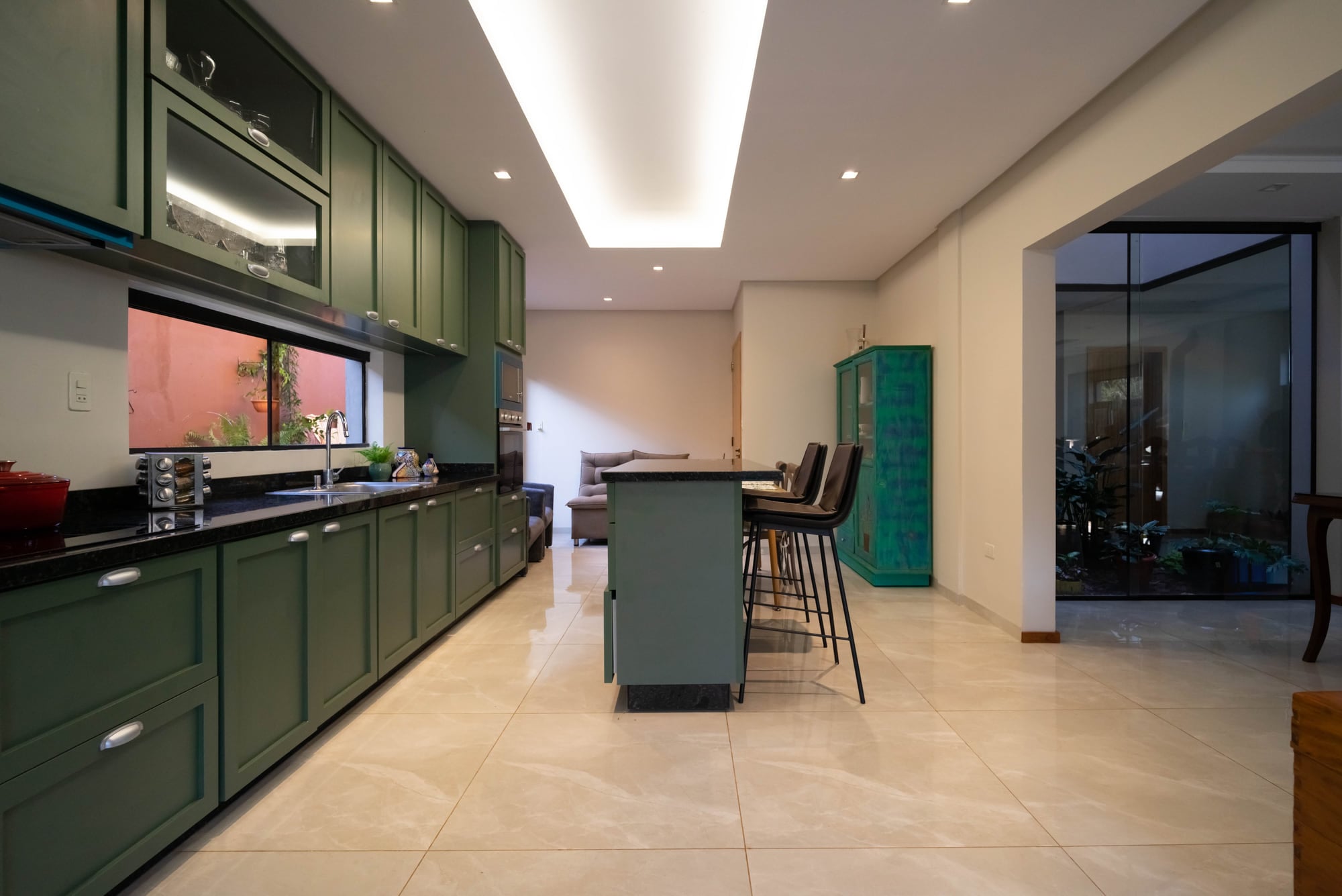 Cocina integrada con muebles verdes, isla con banquetas y living al fondo